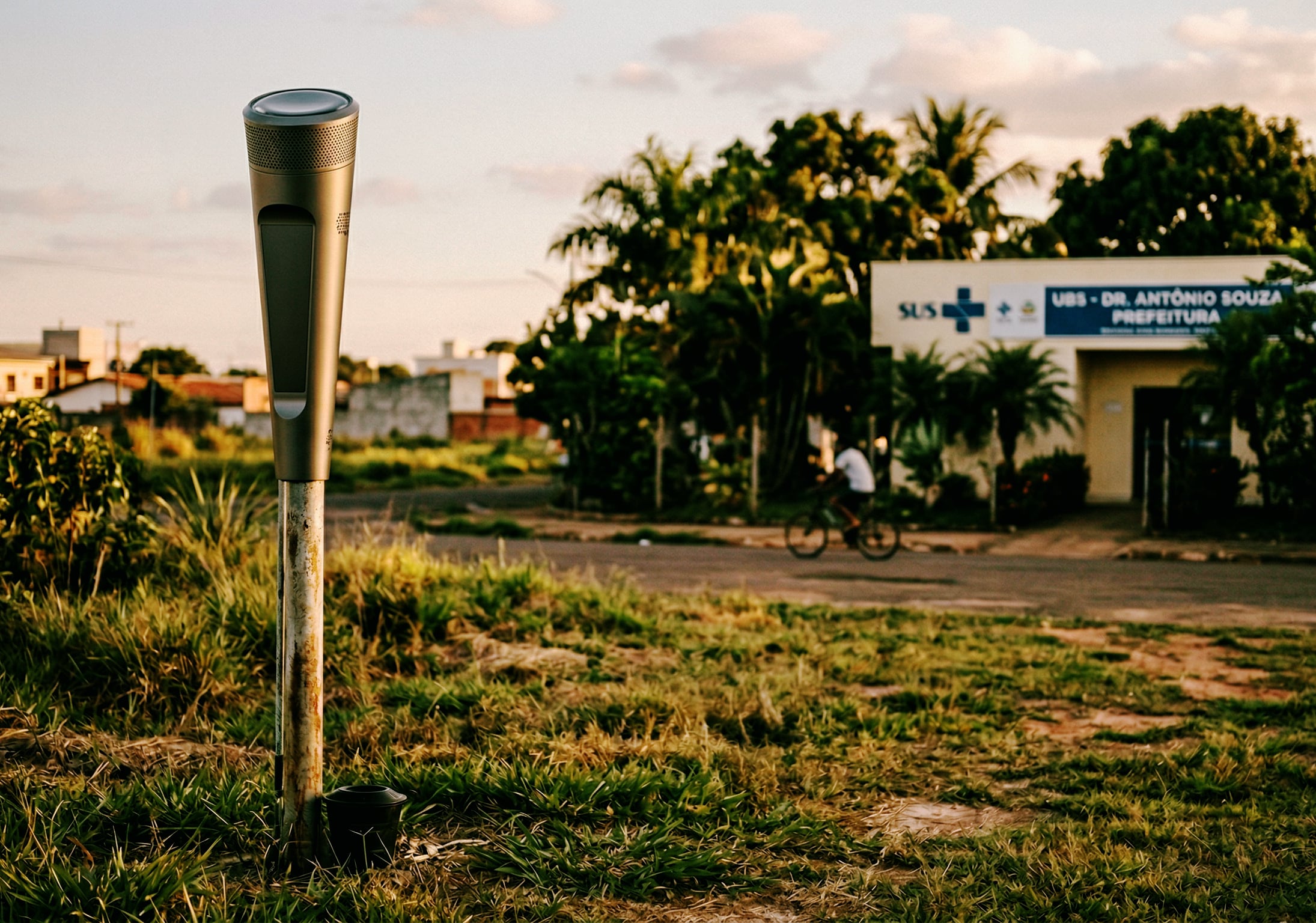 Pluviômetro em campo aberto com UBS do SUS ao fundo em cidade brasileira